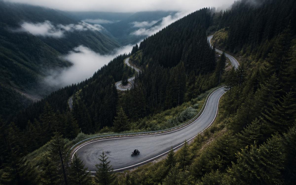 Misty mountain pass with hairpin switchbacks through dark coniferous forest